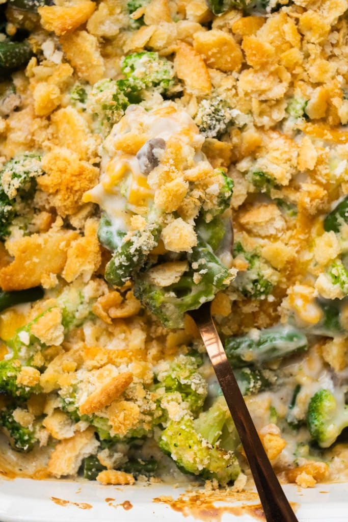 spoon on top of green bean and broccoli casserole with melted cheese and ritz crackers on top.