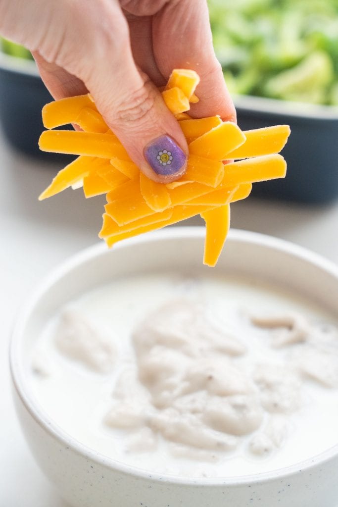 hand sprinkling cheese into bowl with purple nail polish on.