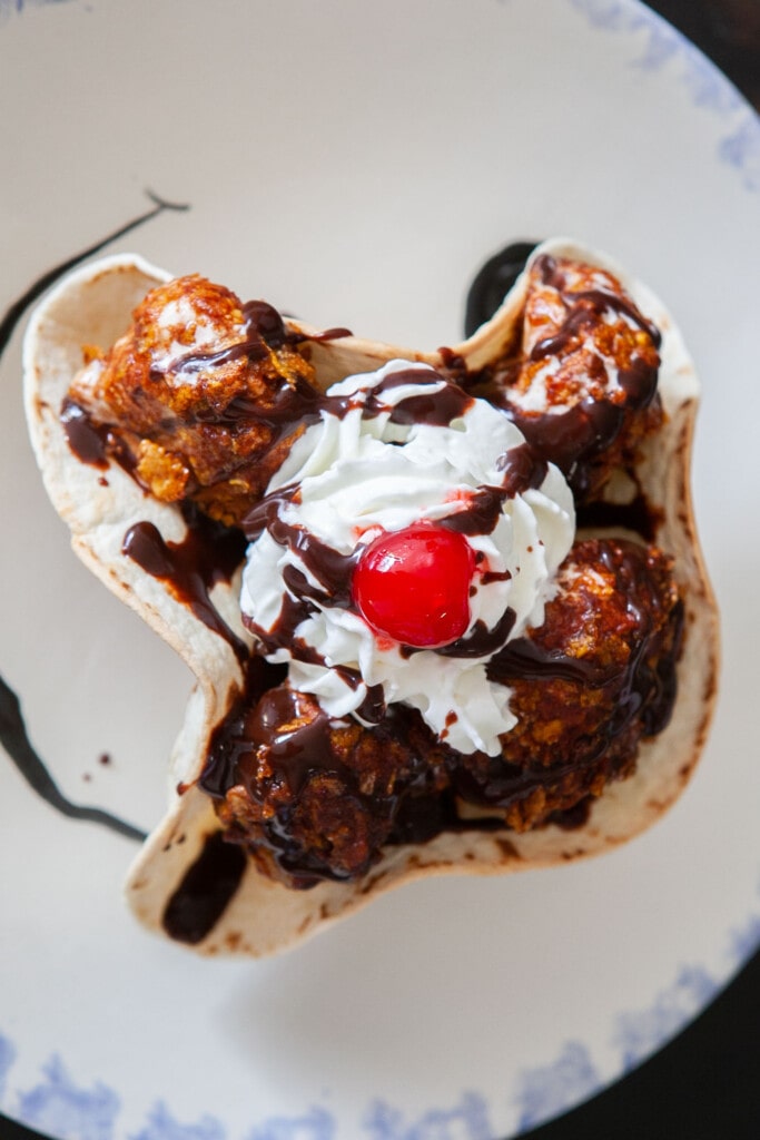 fried ice cream with whipped cream, chocolate syrup and cherry in tortilla shell bowl.