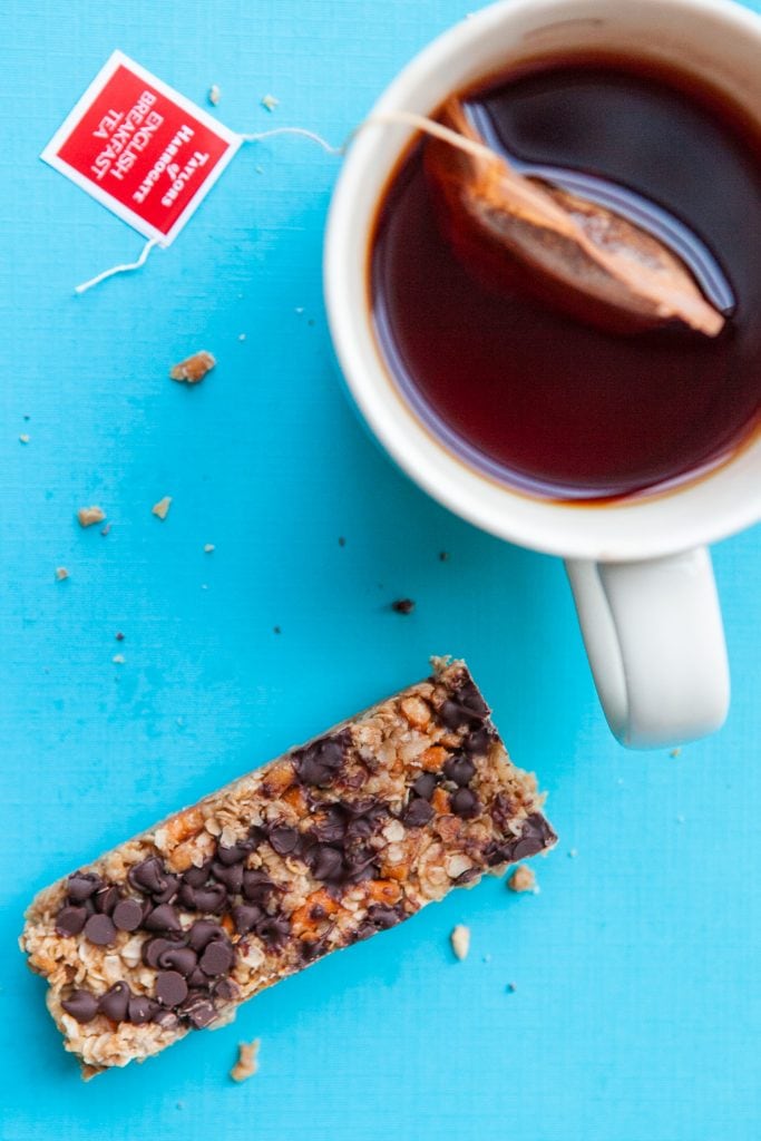 peanut butter granola bar on blue background next to white mug filled with tea.
