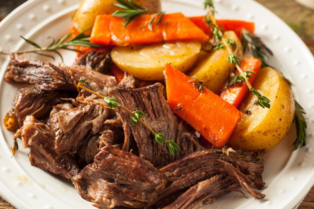 pot roast with potatoes and carrots and springs of thyme on top on white plate