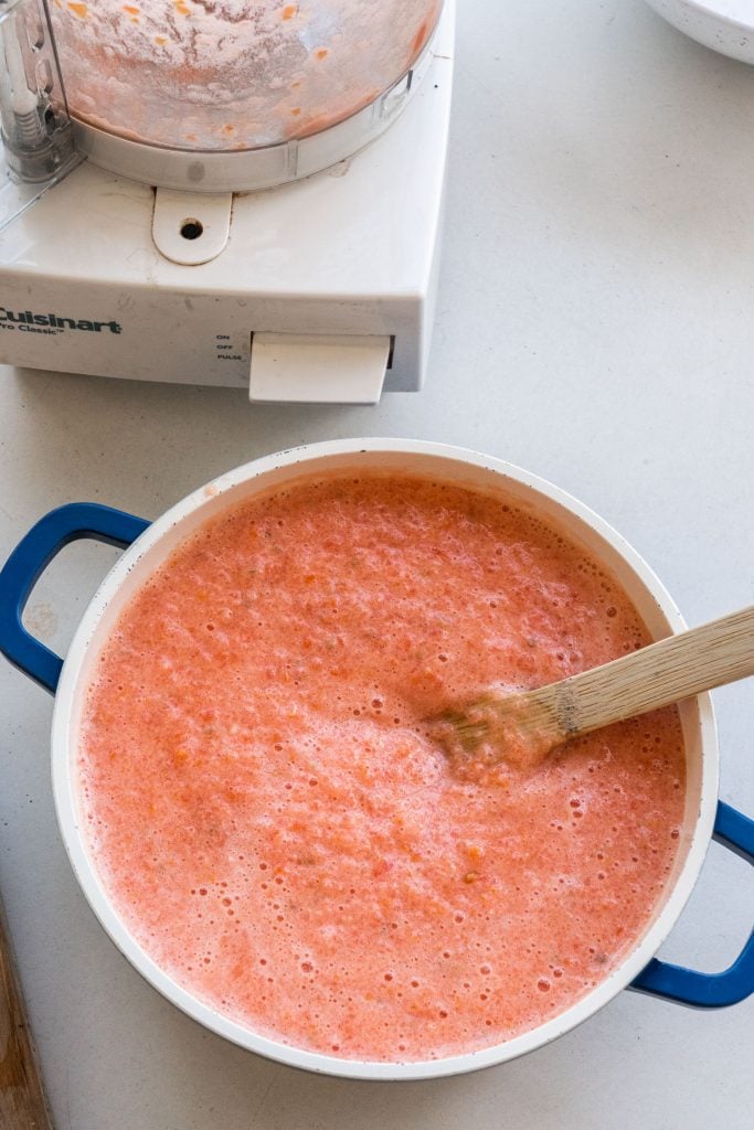 tomato liquid in soup pot next to food processor on table.