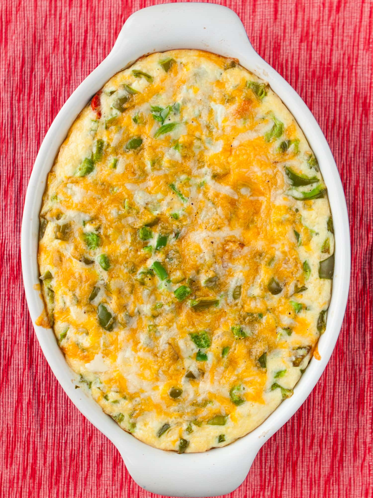 green pepper casserole in baking dish on red table background.