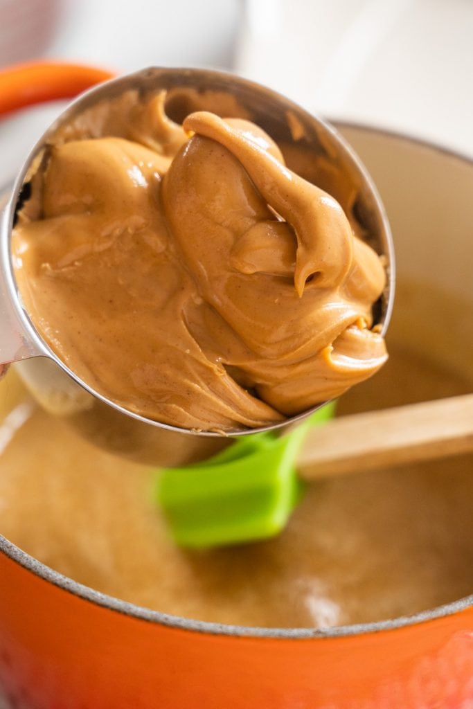 measuring cup filled with peanut butter over saucepan.