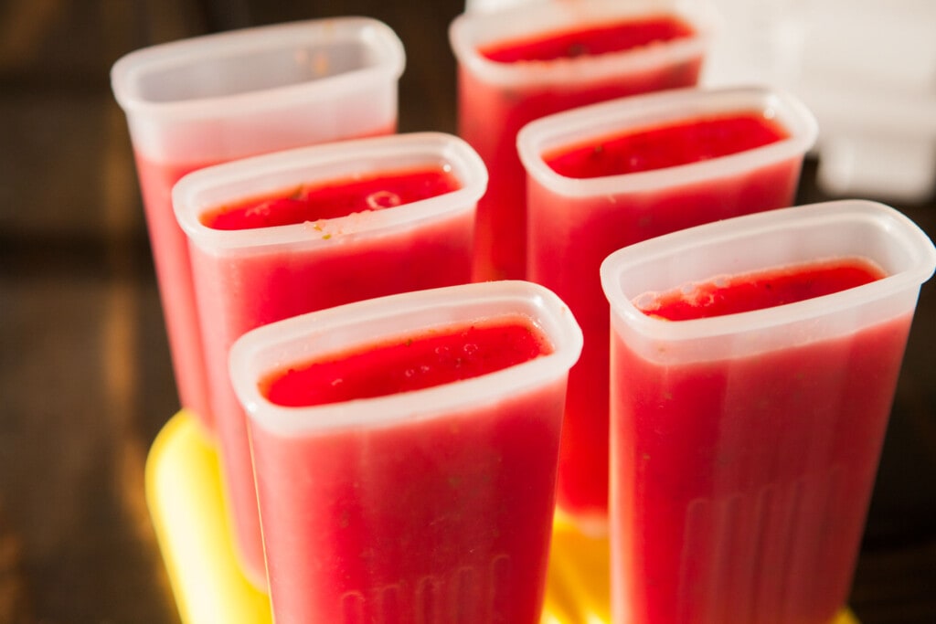 popsicle molds on brown table filled with watermelon puree. 