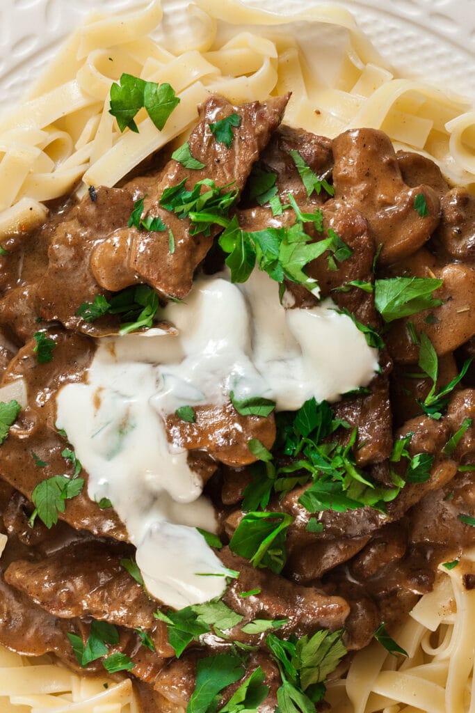 plate of egg noodles with beef stroganoff and sour cream on top.