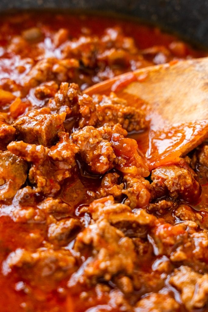 spoon stirring saucy ground beef that has enchilada sauce and salsa in it.