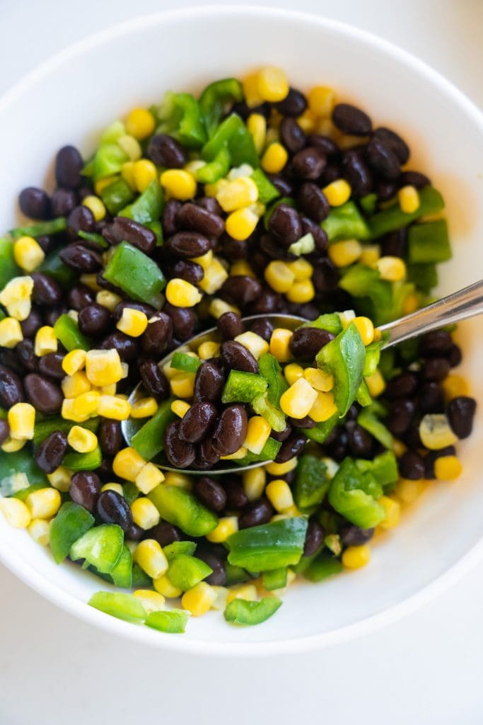 mixing bowl filled with beans, corn and green peppers.