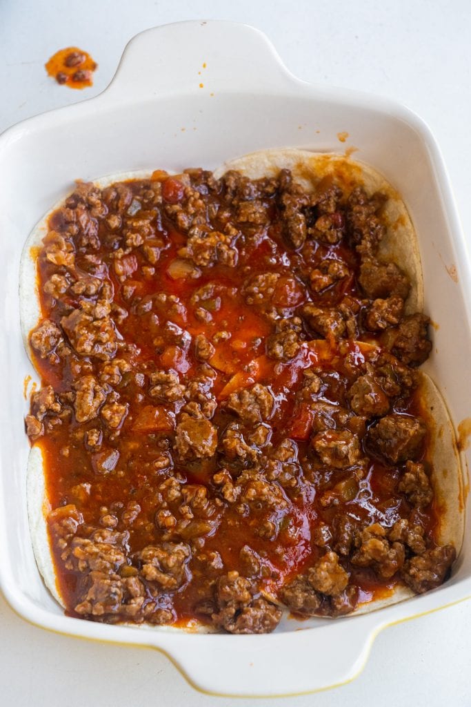 ground beef on top of tortillas in baking dish.