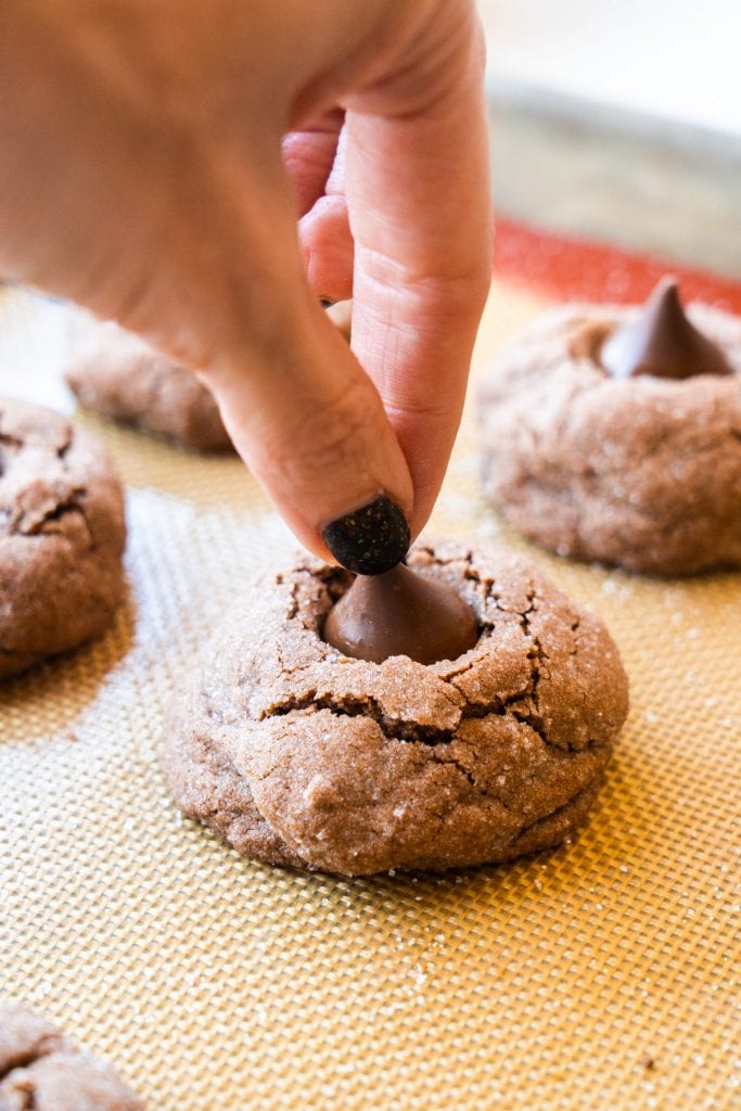 hand pressing down hershey kisses gently into cookies on baking sheet.