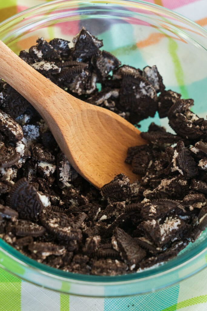 crushed up oreo cookies in glass bowl with spoon crushing them.