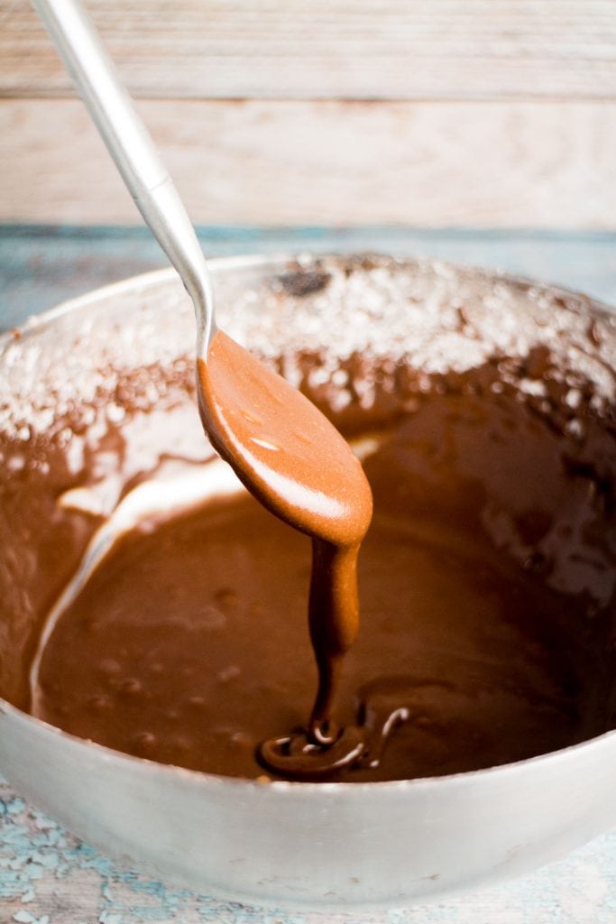 spoon dipping into bowl with chocolate frosting.