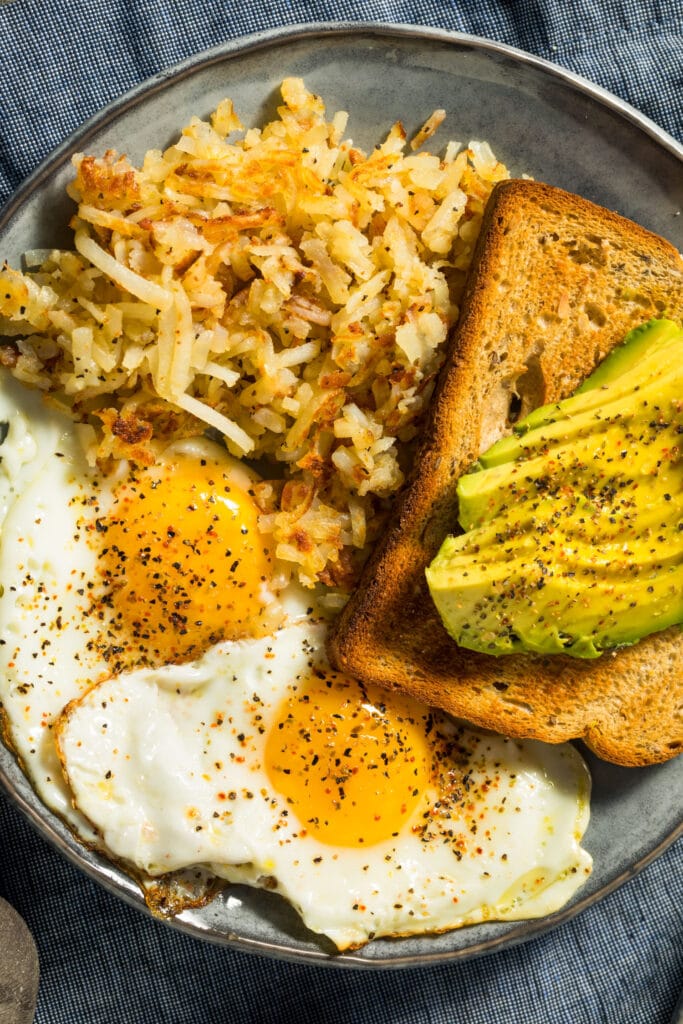 hash browns next to toast, avocado adn eggs for breakfast.