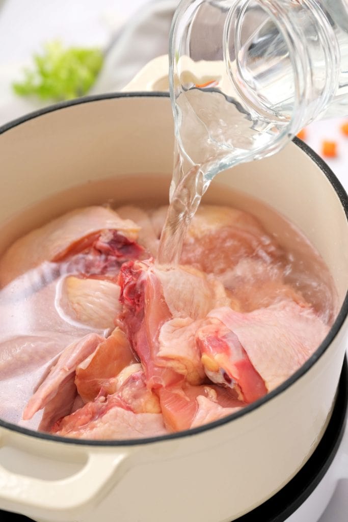 water being added on top of chicken in large pot.