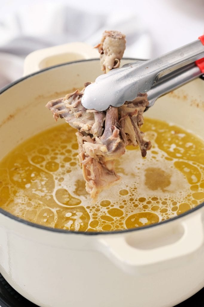 chicken bones being removed from soup pot with tongs.