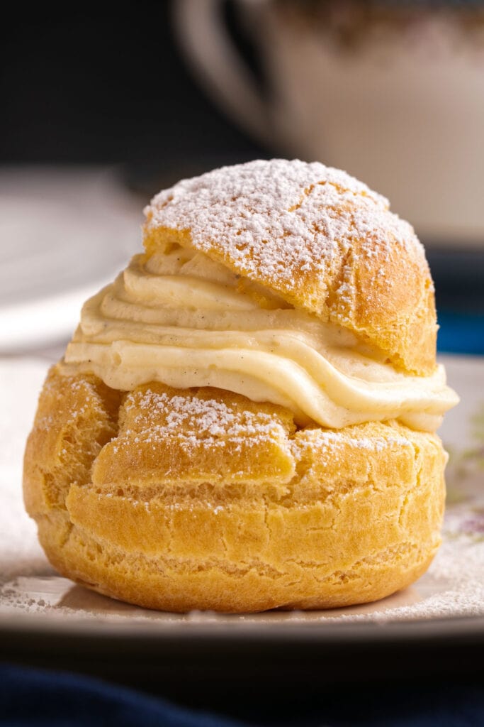 closeup of cream puff with pudding filling inside with powdered sugar on top.