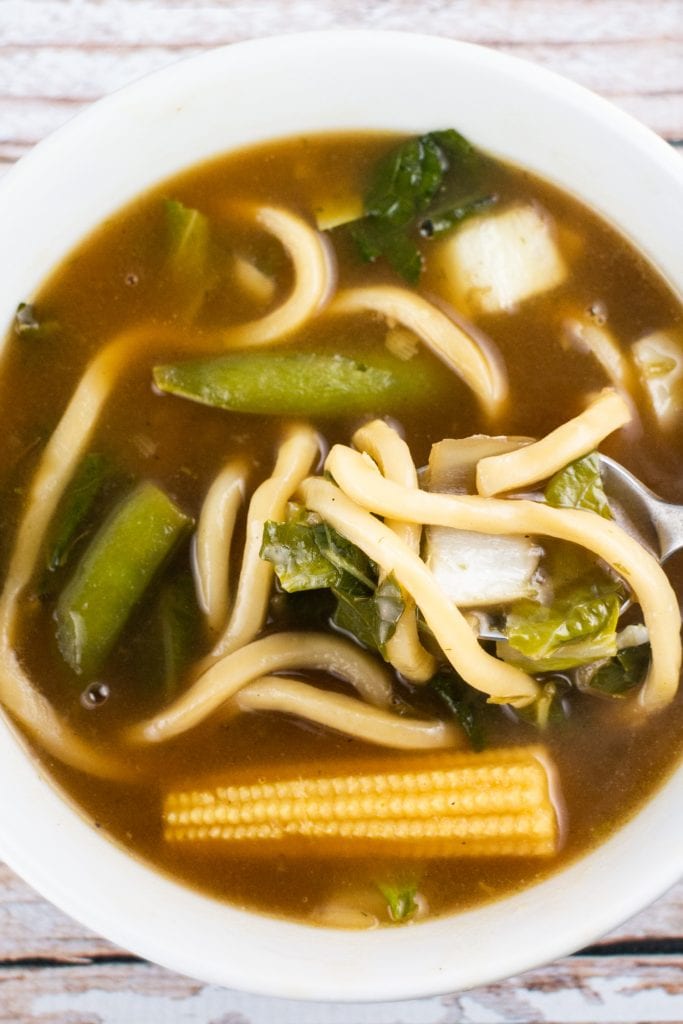 bowl of udon noodle soup with corn, peas and bok choy.