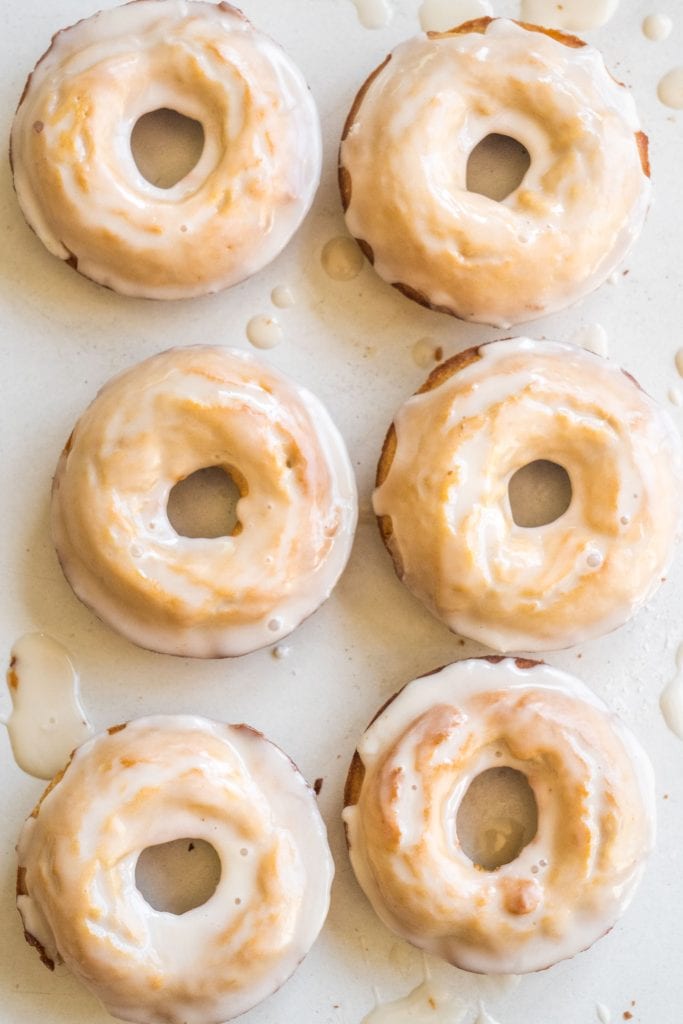 6 peanut butter donuts with white vanilla glaze sitting on white table.