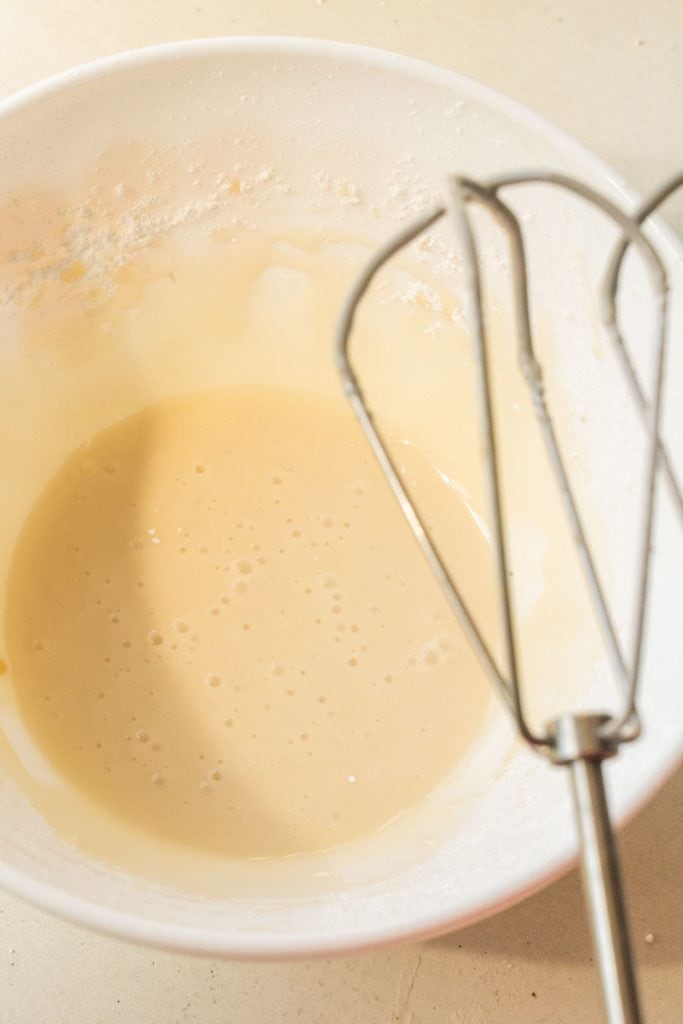 vanilla glaze in white bowl with mixer sitting above it.