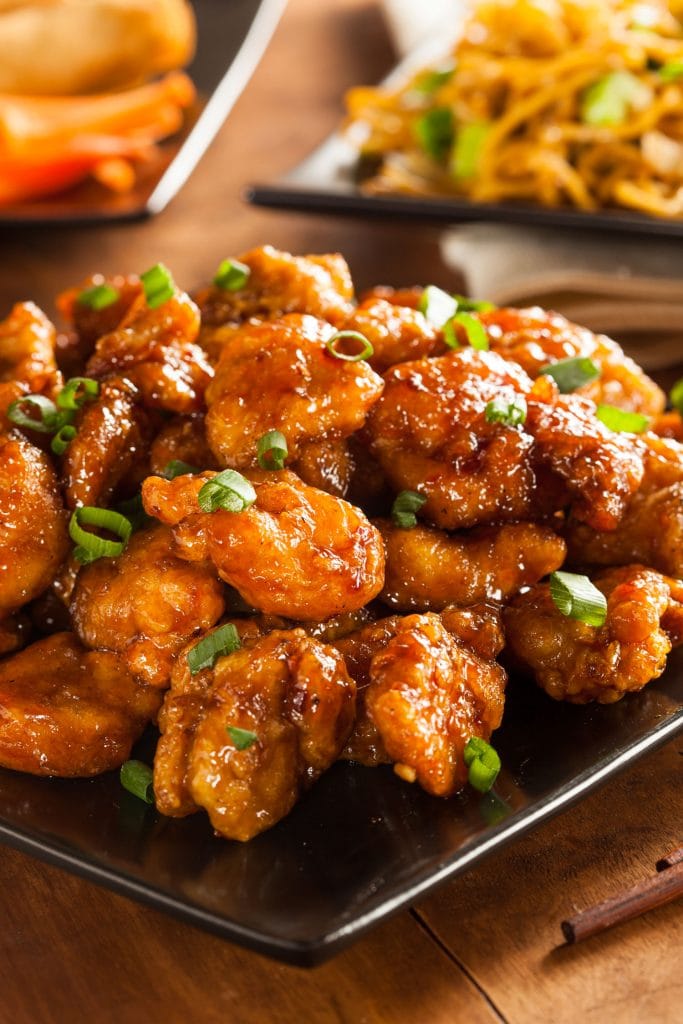 general tsos chicken on plate with lo mein behind it.