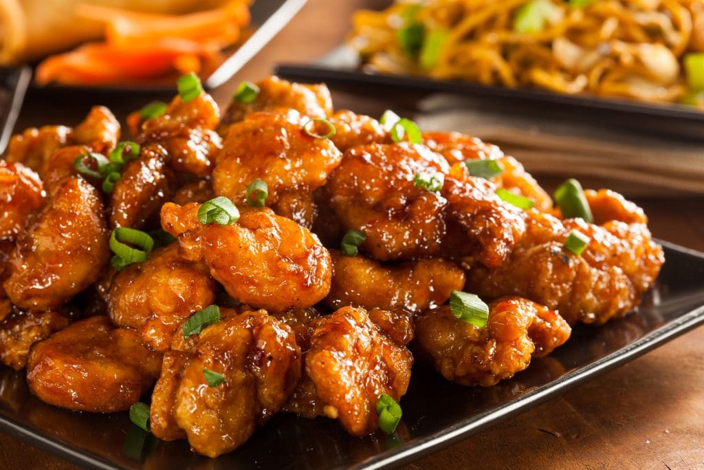 general tsos chicken on black plate with other side dishes in back.