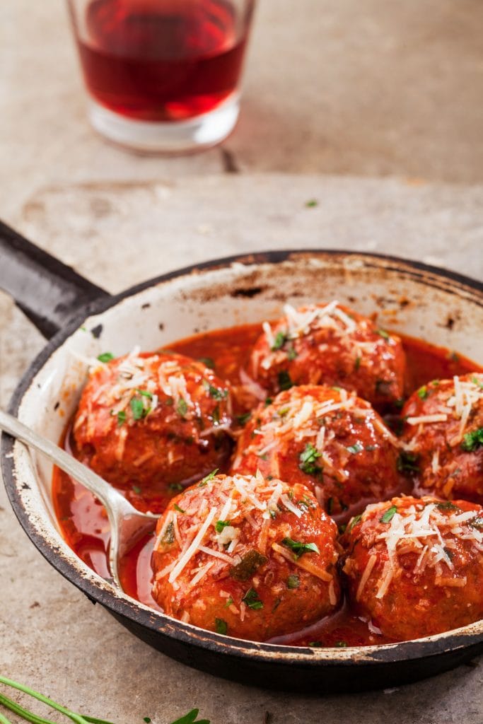 meatballs covered in tomato sauce with parmesan cheese on top in pan.