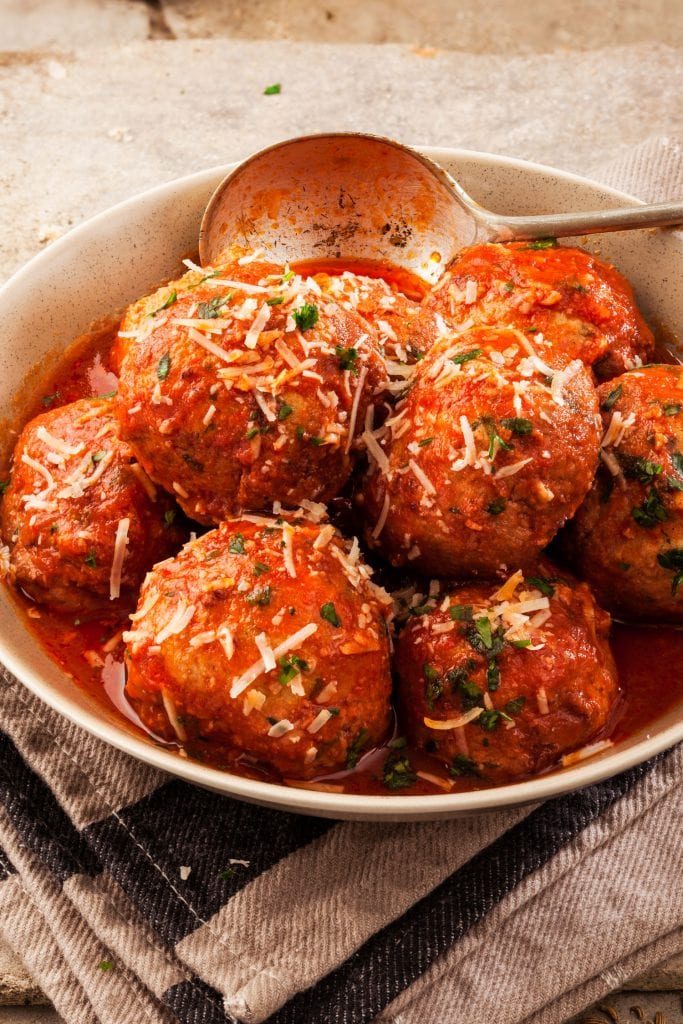 kale meatballs in bowl covered with tomato sauce.