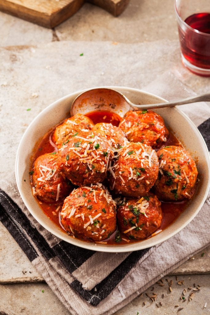baked meatballs with kale in tomato sauce in rustic bowl. 