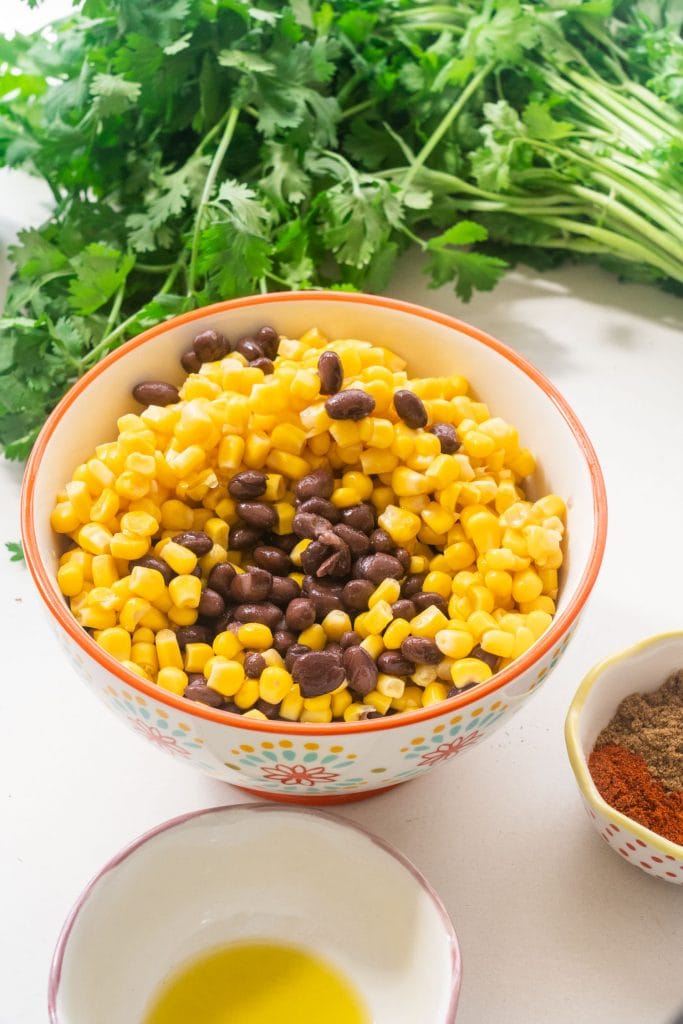 big bowl filled with corn and black beans, olive oil and spices in smaller bowls  around big bowl.