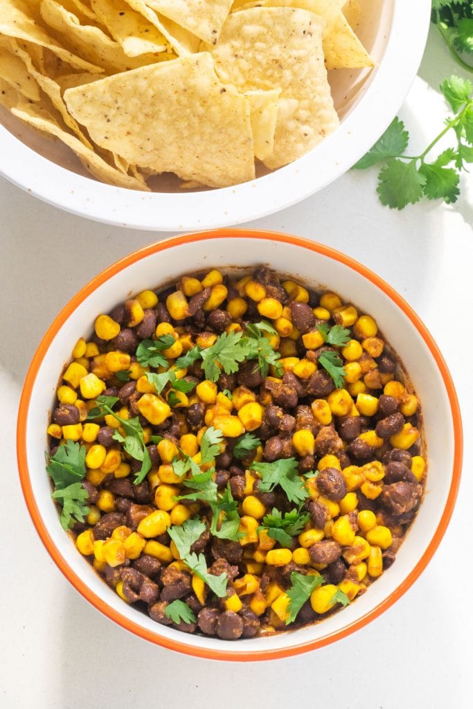 bowl filled with black bean corn salsa with cilantro on top, next to bowl of tortilla chips.