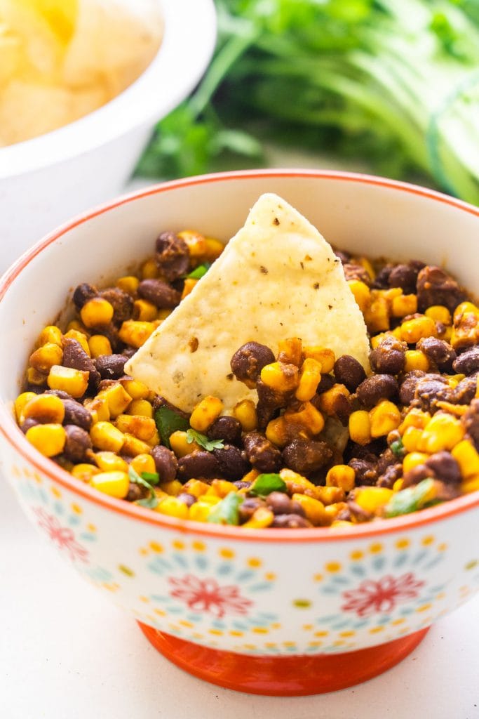 tortilla chip in bowl of black bean corn salsa.