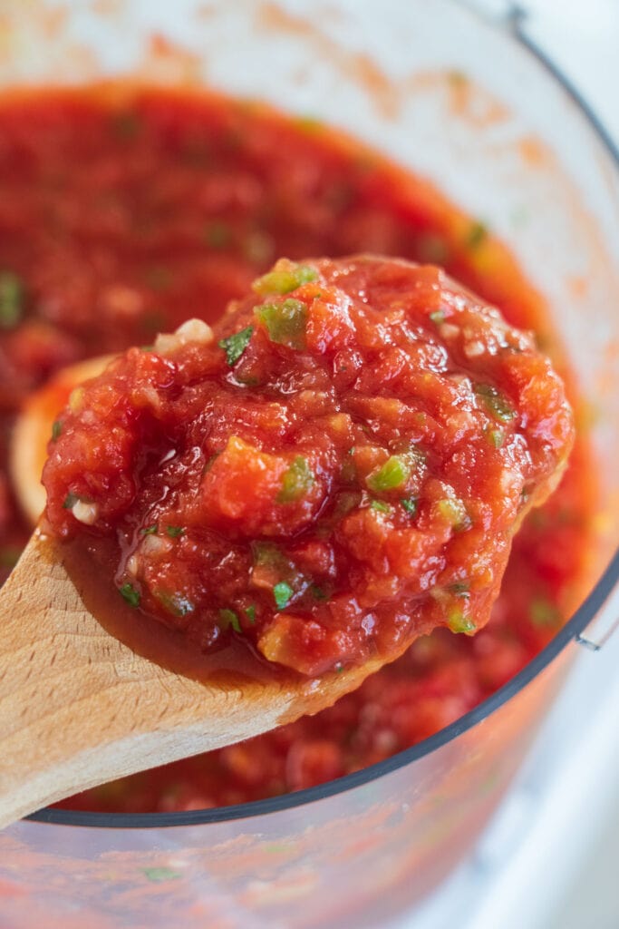 wooden spoon lifting salsa out of food processor.