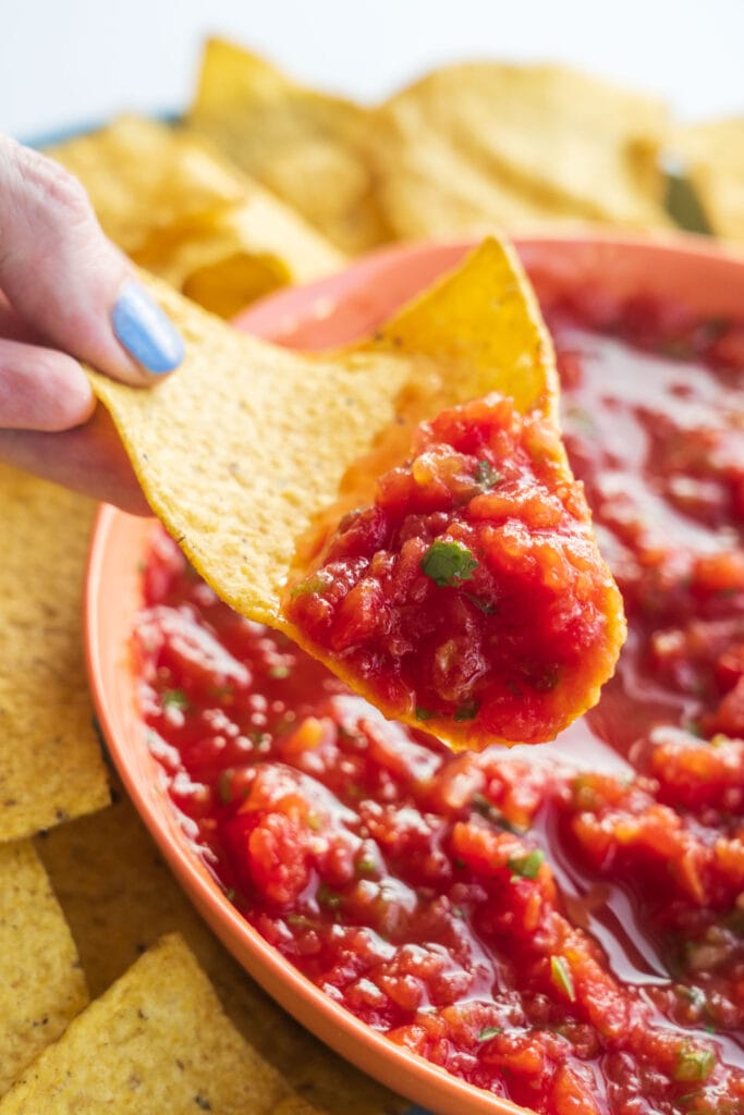 hand scooping salsa on tortilla chip out of bowl. 