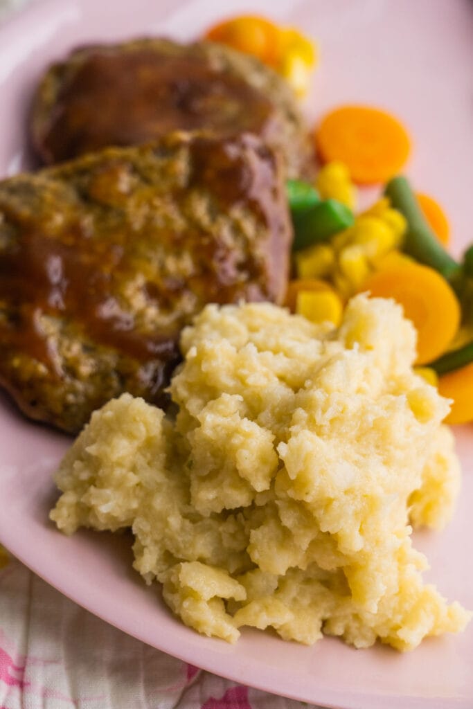 cauliflower served next to meatloaf and vegetables on pink plate.