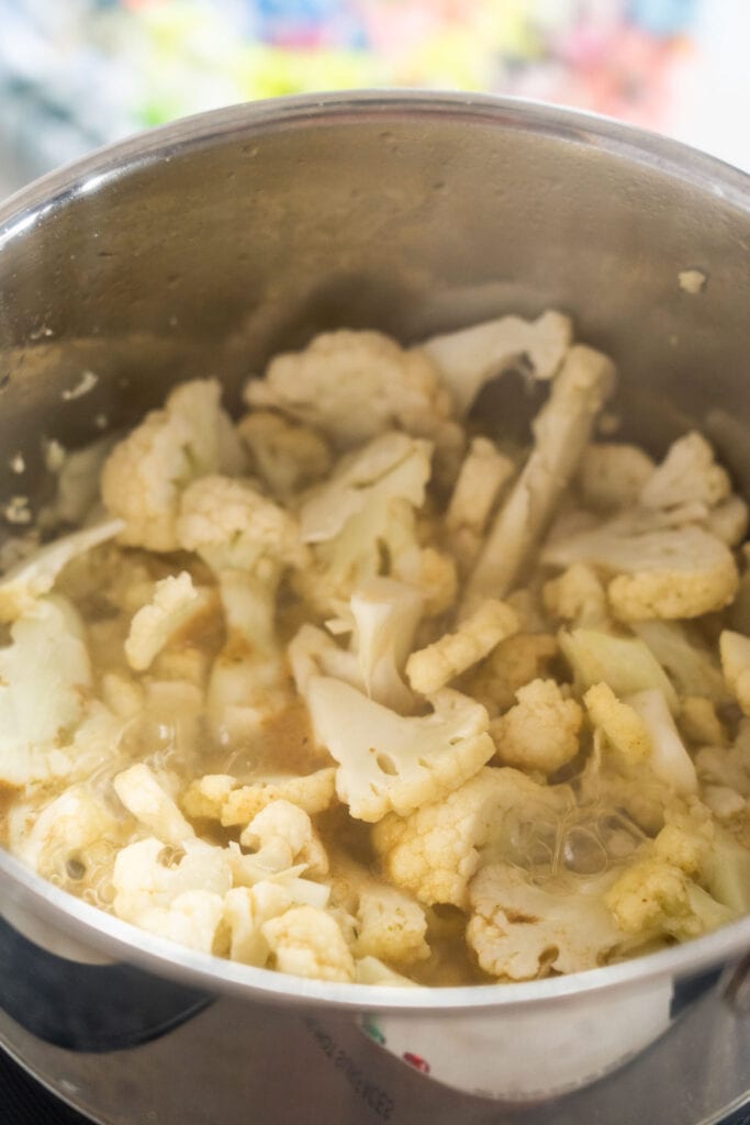 cauliflower boiling in chicken broth in saucepan.