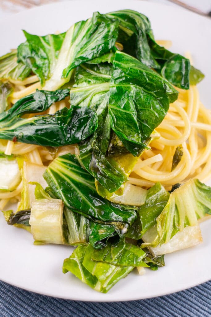 sauted garlic bok choy over pasta on plate.