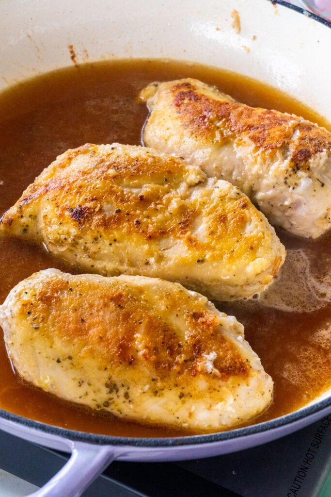 fried chicken in pan with broth and marsala cooking wine in it.