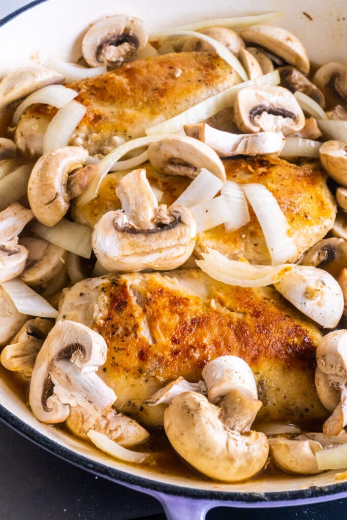 mushrooms and onions on top of chicken in pan.
