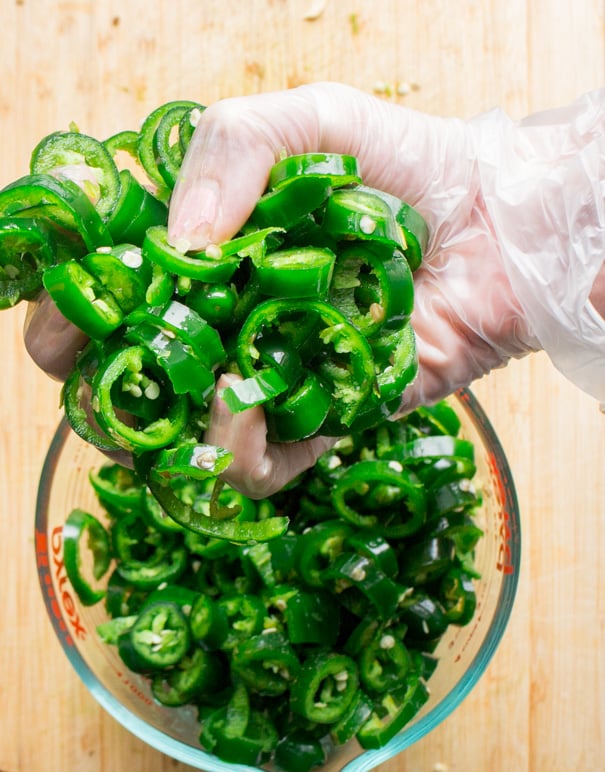 Hands wearing gloves slicing jalapeno hot peppers