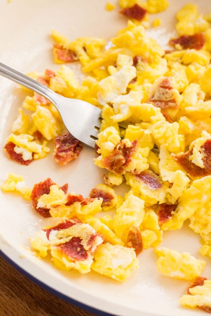 scrambled eggs with bacon in skillet with fork
