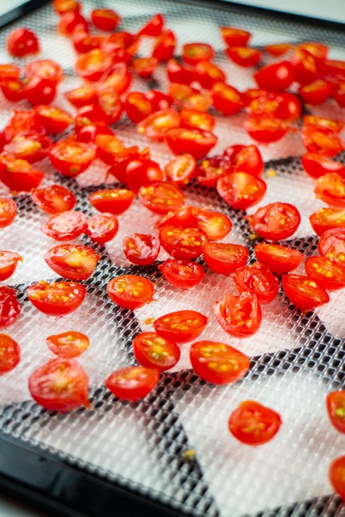 cherry tomatoes cut in half on dehydrator sheet.