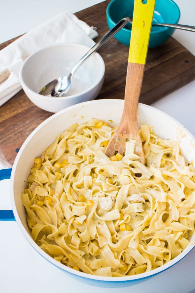large pot filled with creamy egg noodles, chicken and corn on table, with wooden spoon in it.
