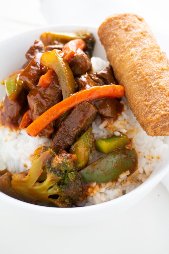 beef, vegetables and rice in bowl next to egg roll.