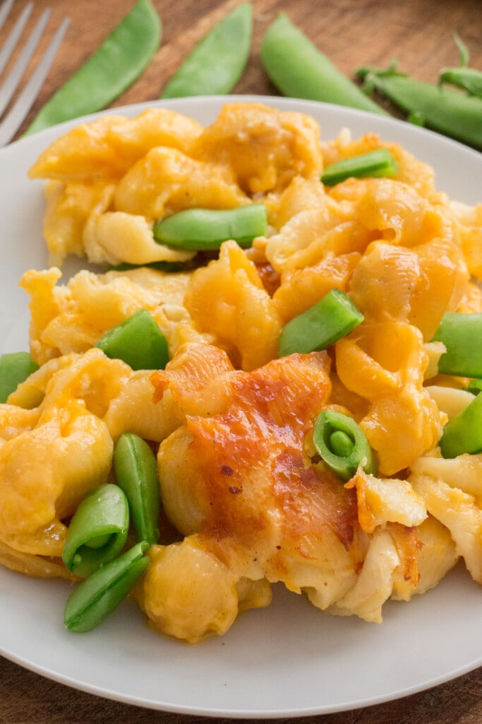 closeup of macaroni and cheese with peas on white pltae.