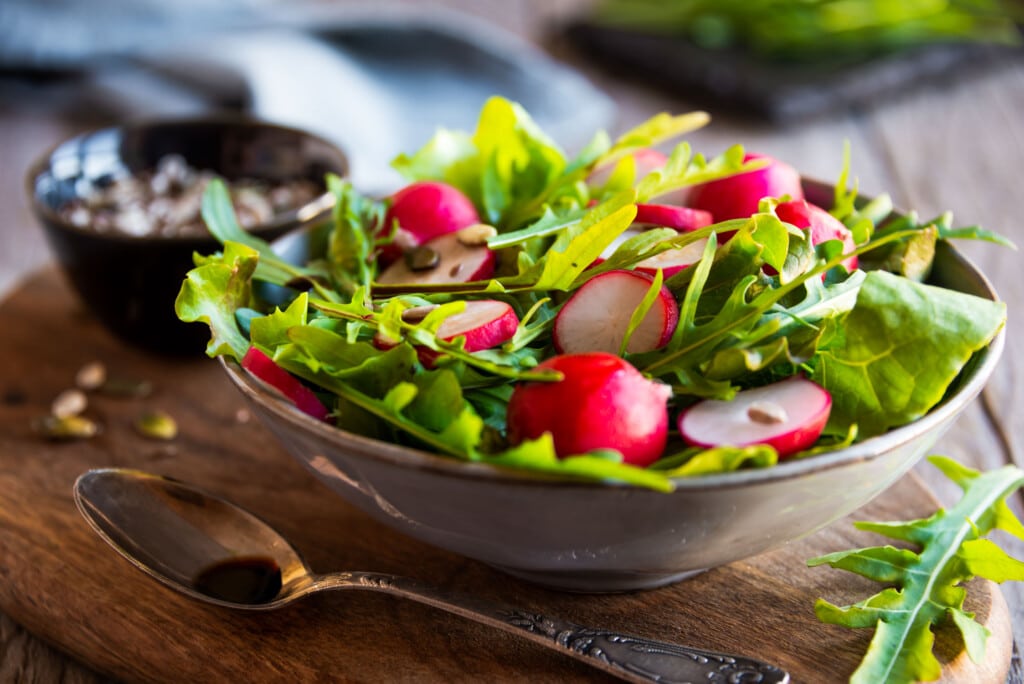 arugula and radish salad in bowl on table.
