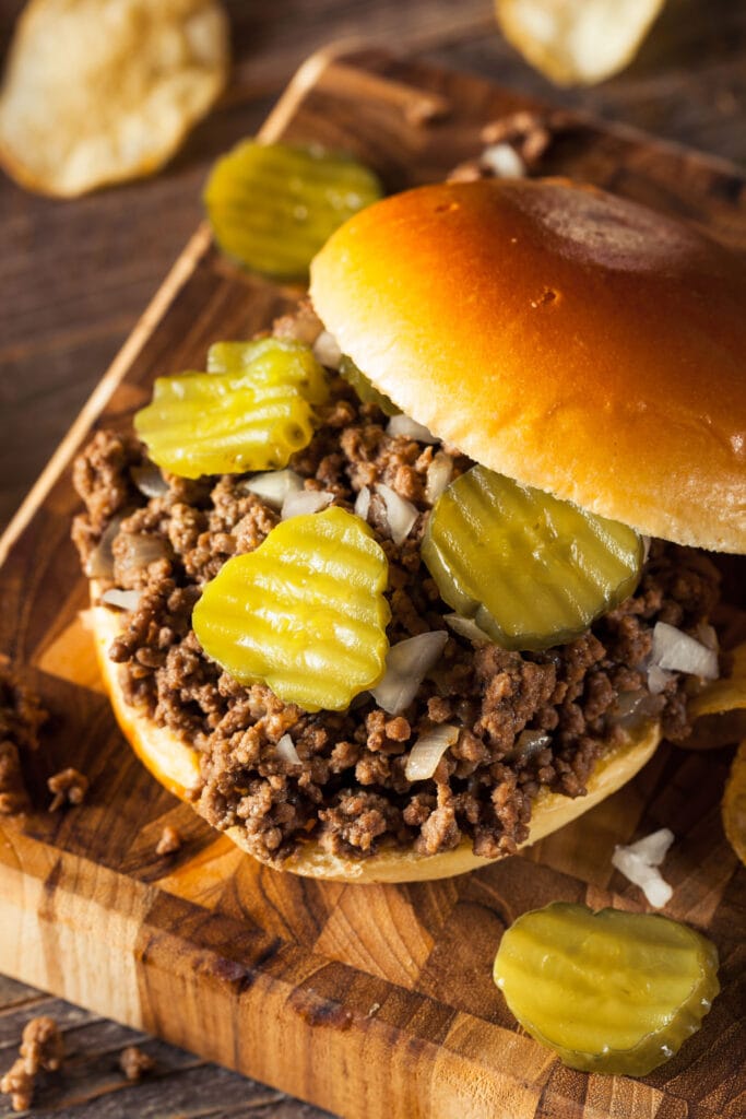 dill pickles on hamburger meat on bun with onions.