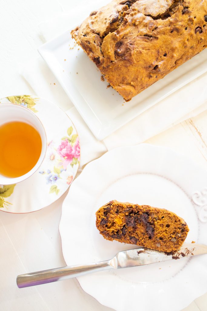 slice of carrot bread on white plate next to cup of tea.