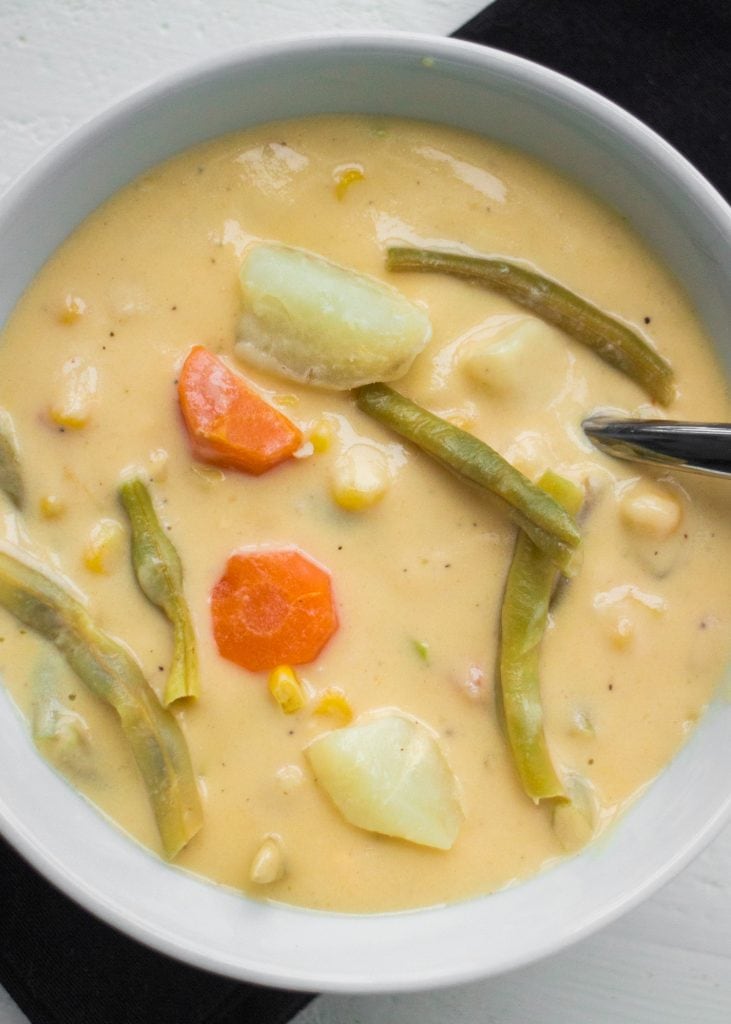 cheesy vegetable soup with potatoes, green beans and carrots in white bowl.