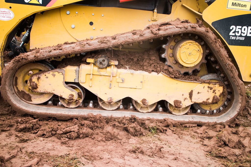 Close-up of a yellow construction vehicles muddy rubber track and wheels on soft, wet ground, showing the mechanical details and texture of the treads and soil.
