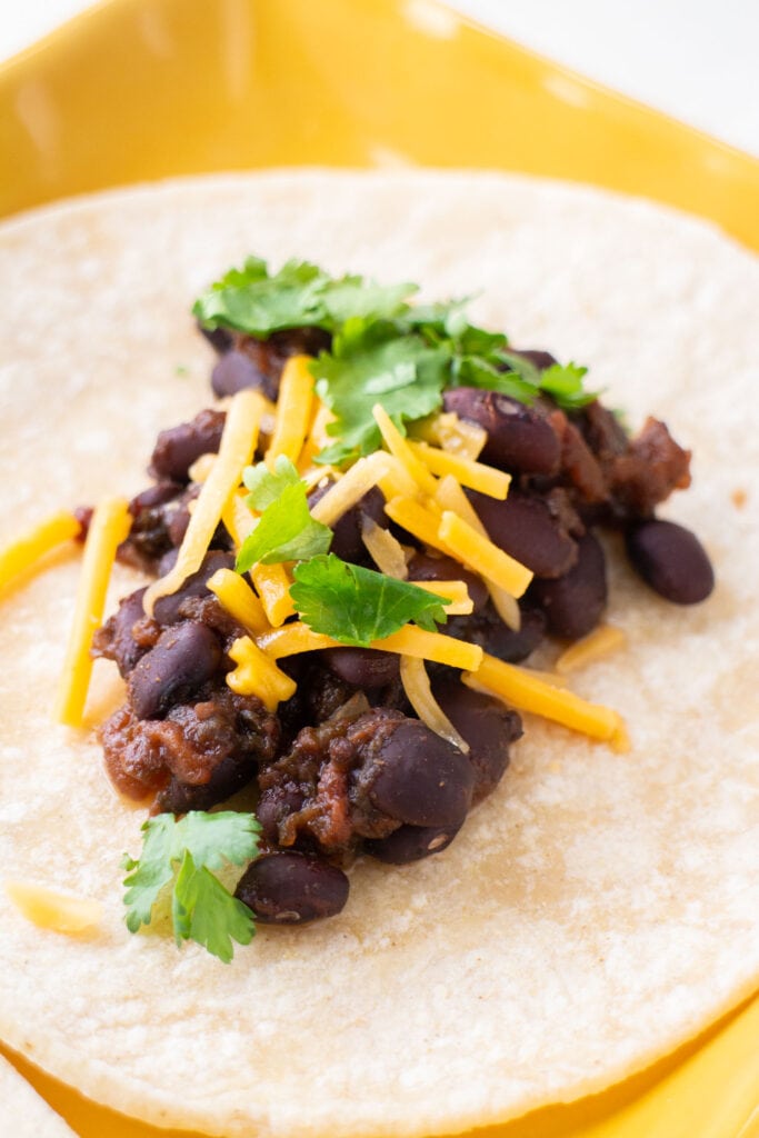 black beans on tortilla on yellow plate.